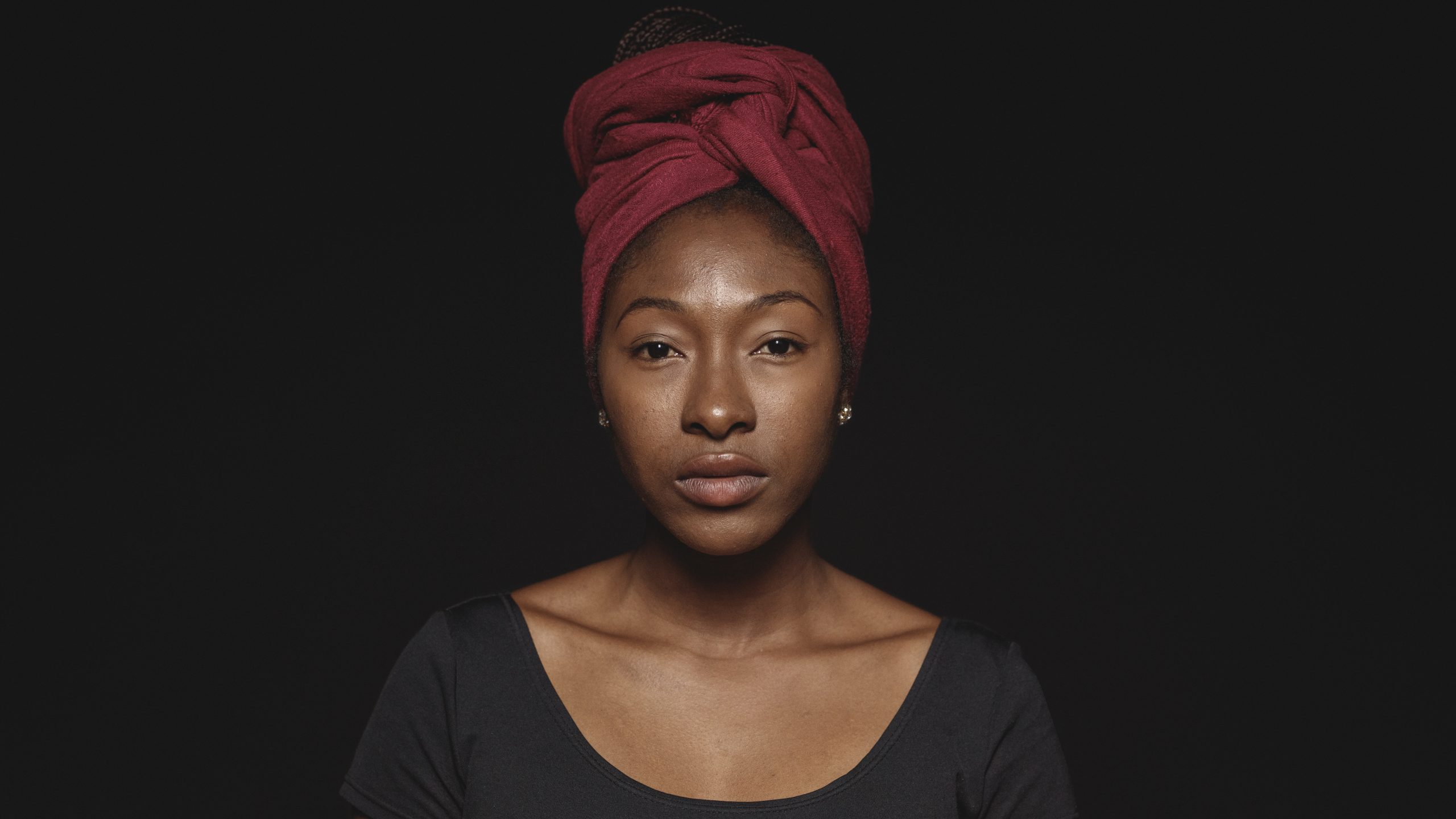 Close up of african woman isolated on black background. African female with a scarf wrapped on head looking at camera.